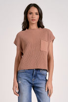Woman wearing a brown ribbed top with a pocket and blue jeans on a white background