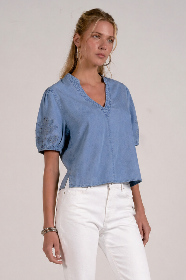 woman showing a slight side view of chambray embroidered sleeve top paired with white denim