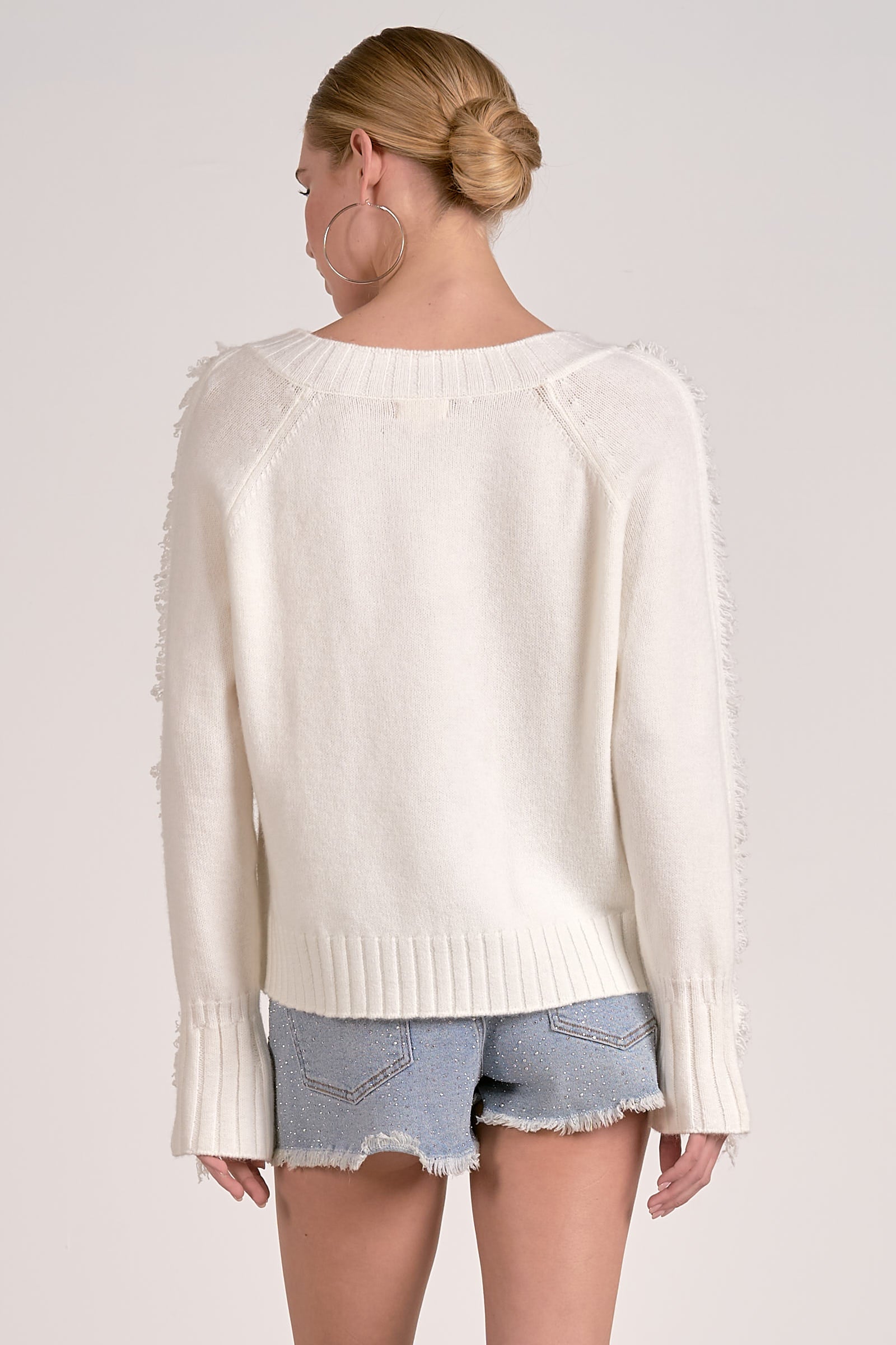 Model showing back of Willow Fringe V-Neck Sweater in ivory white with fringe trim sleeves from Mainstream Boutique Bloomington