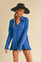 Woman wearing a blue shirt and black hat against a beige background