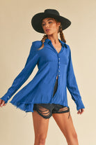 Woman wearing a blue shirt and black shorts with a black hat on a beige background