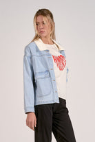 outfit view of light blue denim jacket styled with graphic tee and black pants.