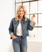 A woman wearing a long sleeve crop jacket with gold-tone buttons and contrast cuffs. The jacket is denim with a medium wash.