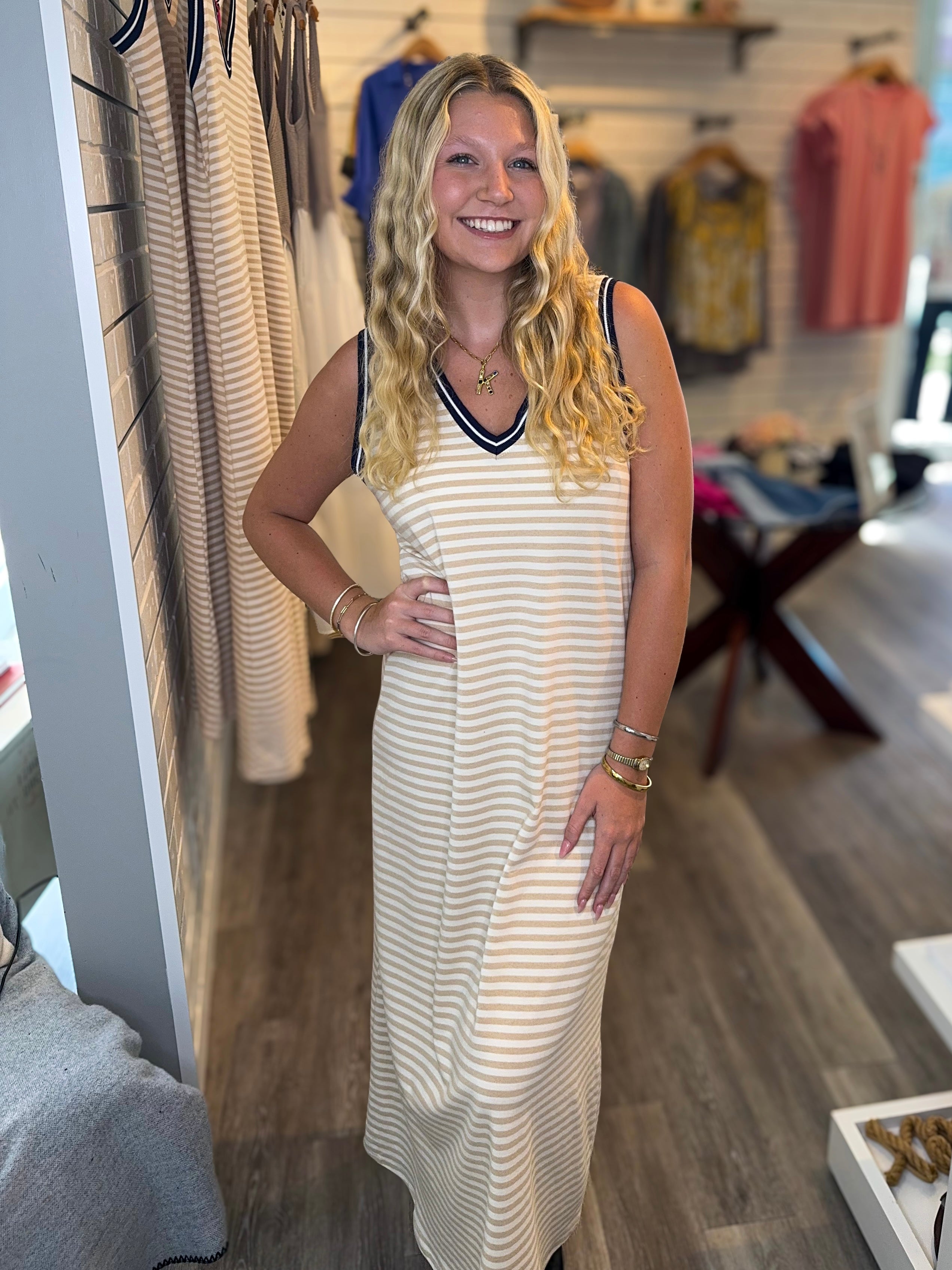 A woman wearing a yellow and white striped maxi dress with a navy v and armhold stripe.