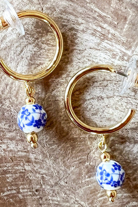 close up of gold hoop earrings with blue and white bead accents on a textured surface