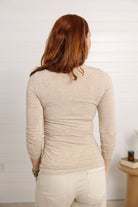 woman showing the back of the mockneck side ruched top in the color brushed tan