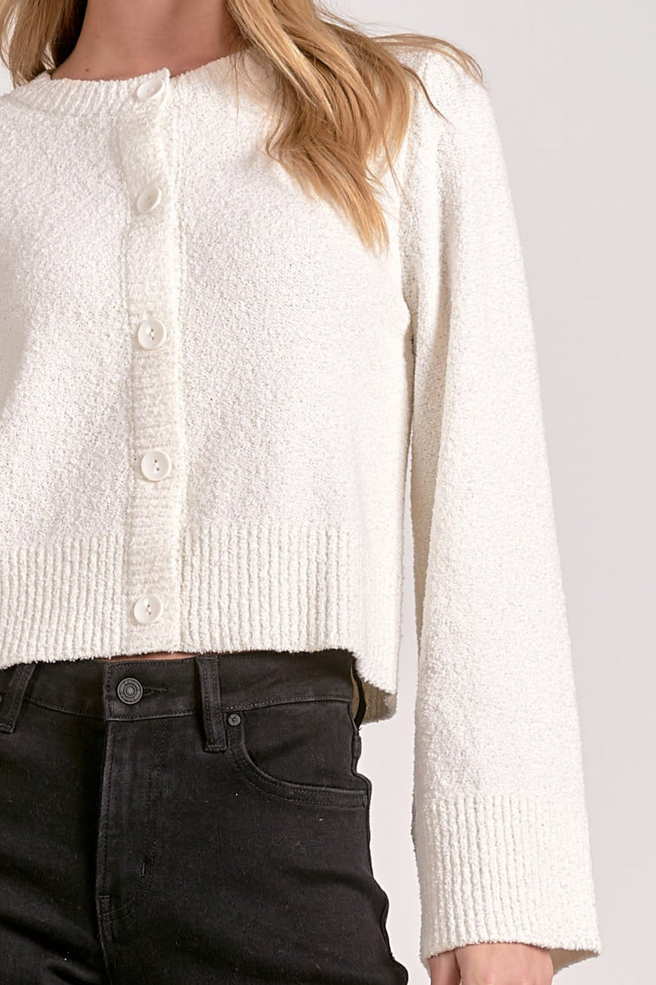Woman showing details on the off white cardigan with flare sleeves.