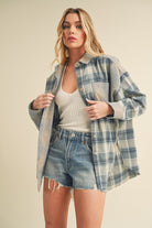 Woman wearing a plaid shirt over a tank top and denim shorts on a beige background