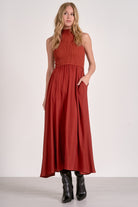 Model wearing rust mockneck sleeveless maxi dress with ribbed bodice, woven skirt, and high-low hem from Mainstream Boutique Bloomington