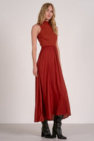 Model wearing rust mockneck sleeveless maxi dress with ribbed bodice, woven skirt, and high-low hem from Mainstream Boutique Bloomington