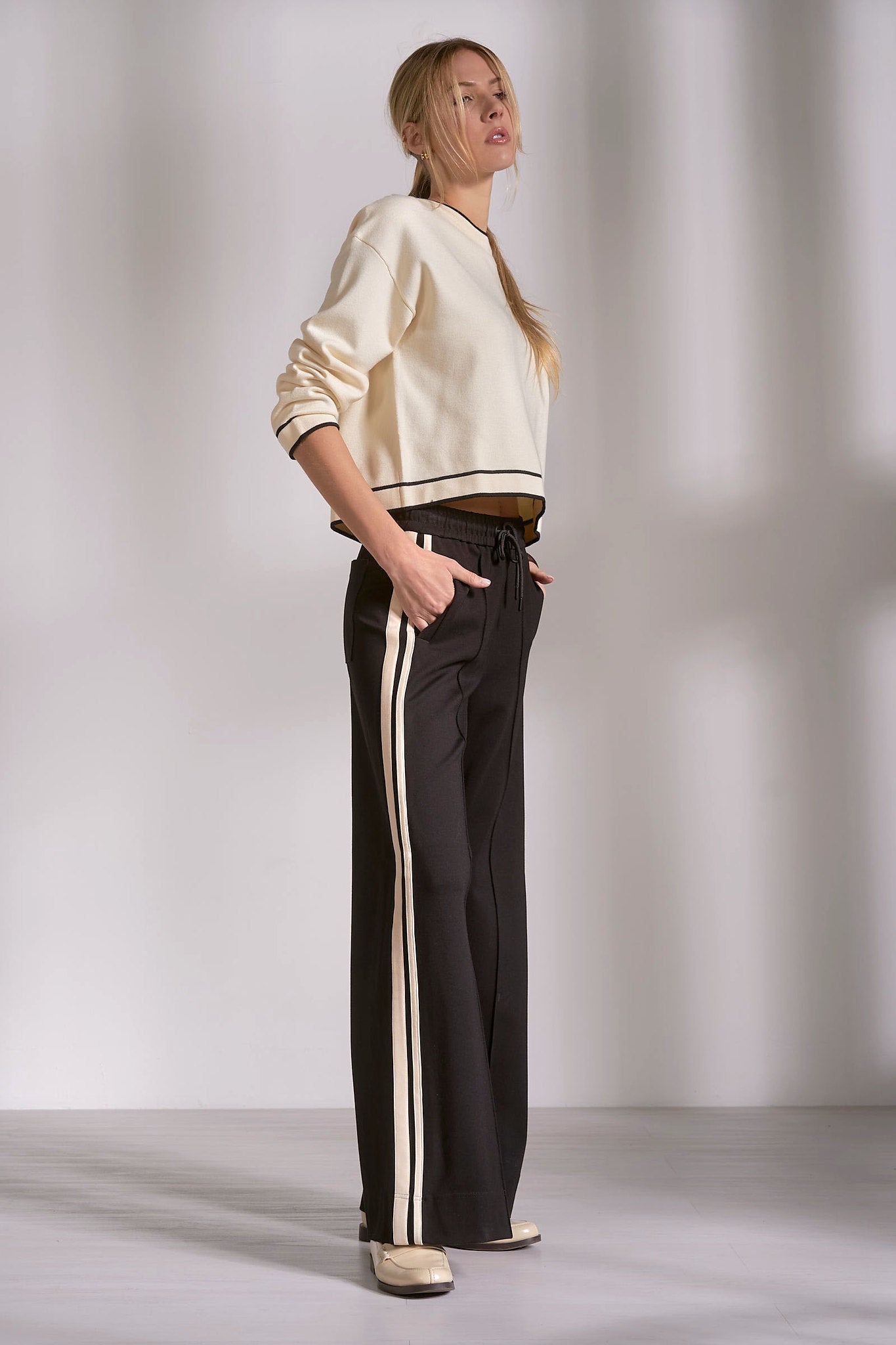 Side view of black track pants with natural stripe and fluid drape