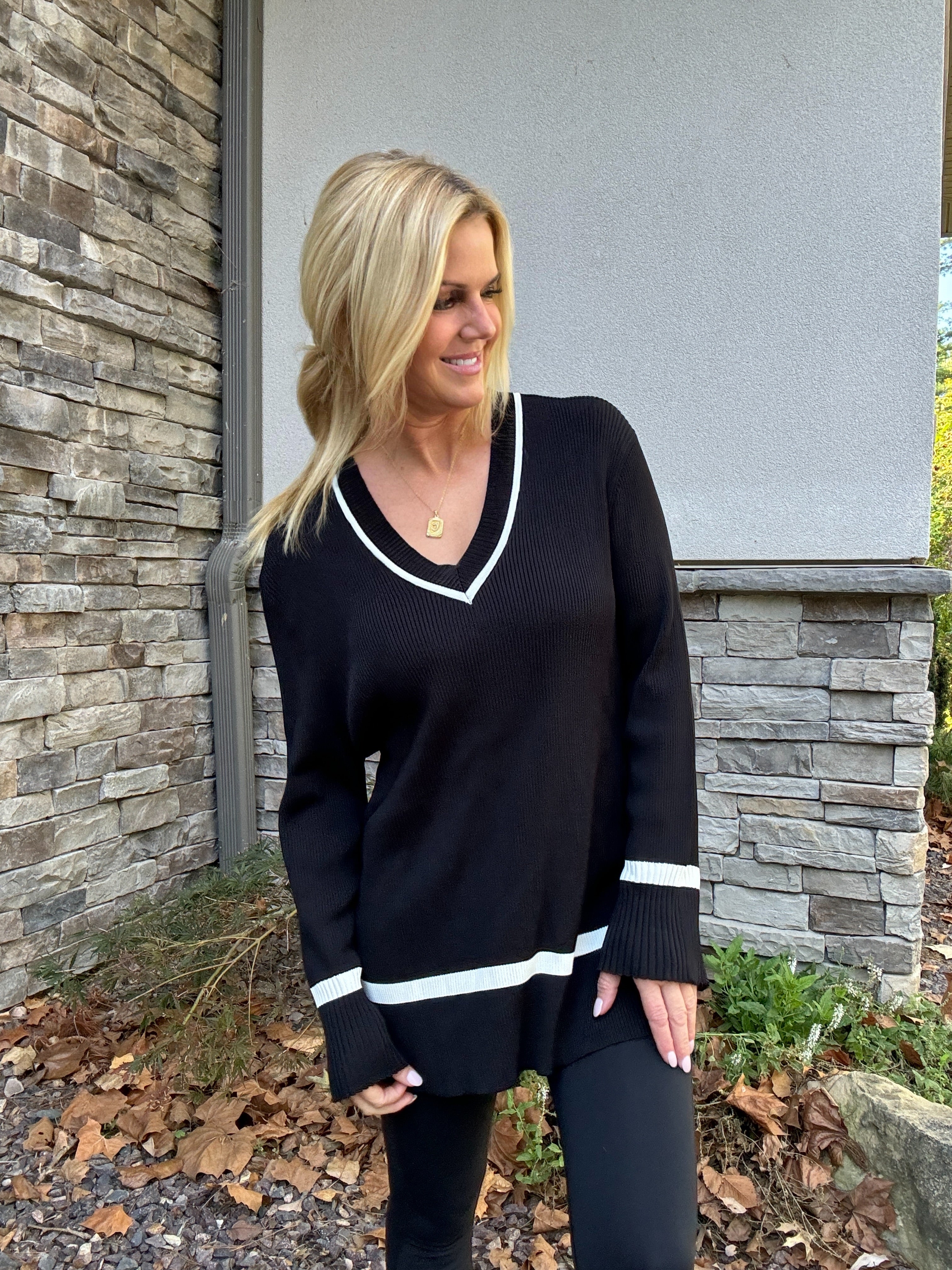 A woman standing outdoors wearing a black knitted track top with white stripes on the sleeves, paired with black pants.
