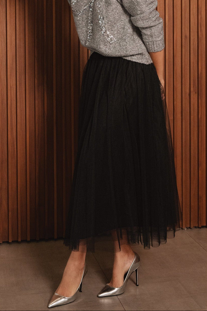 Person wearing a black tulle skirt with a gray sequined top against a wooden paneled wall.