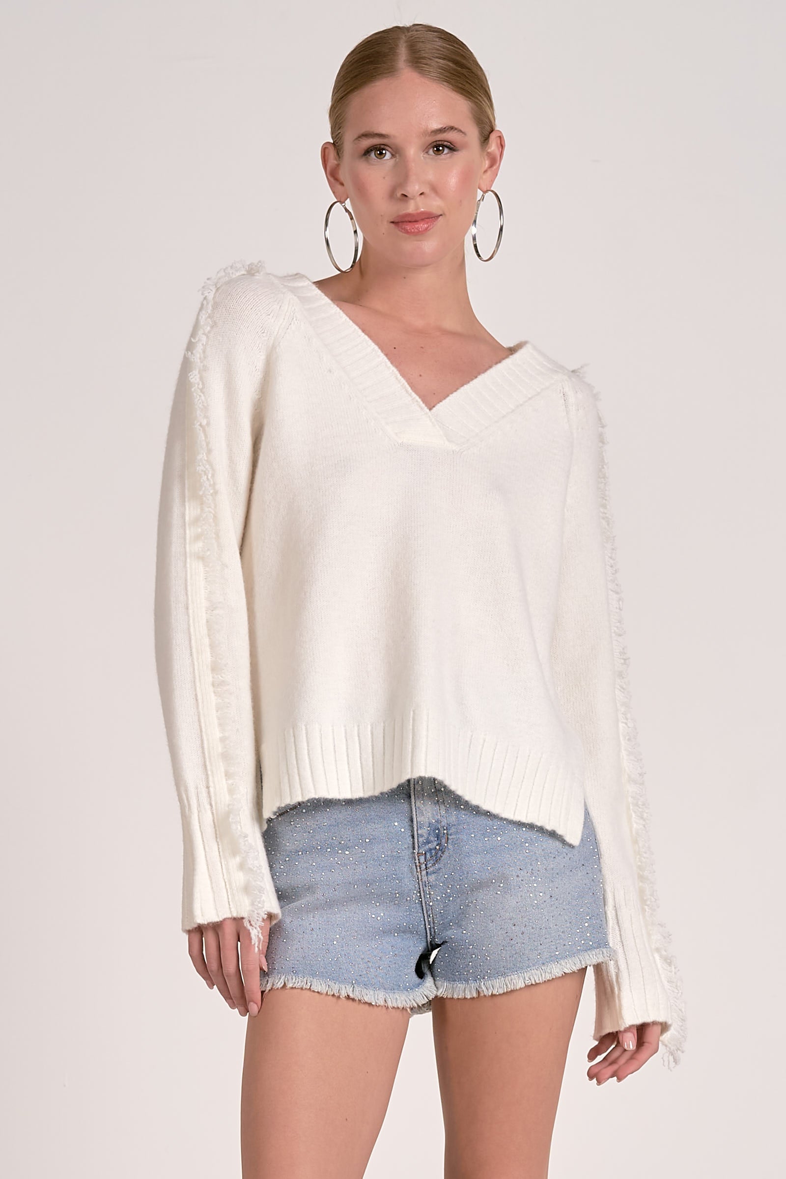 Model wearing Willow Fringe V-Neck Sweater in ivory white with fringe trim sleeves from Mainstream Boutique Bloomington
