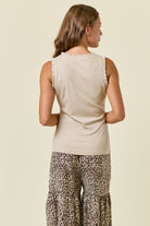 Woman wearing a beige sleeveless top and leopard print pants on a plain background