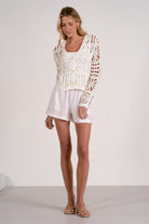 white crochet cardigan with button front and open knit detail styled with white shorts