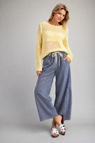 Woman wearing yellow open knit sweater and blue striped drawstring pants